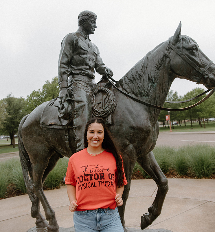 Image of the student contest winner standing in front a statue of a man on a horse, wearing a shirt that says "Future Doctor of Physical Therapy"